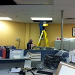 Two staff, one on ladder, cleaning ceiling tiles with a vacuum