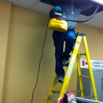 Cleaner on ladder with vacuum cleaning ceiling and titles